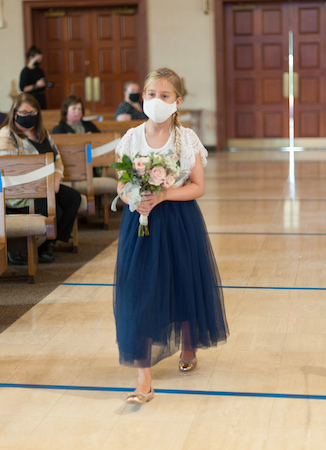 Junior bridesmaid wearing a protective face mask carrying a bouquet of pink roses