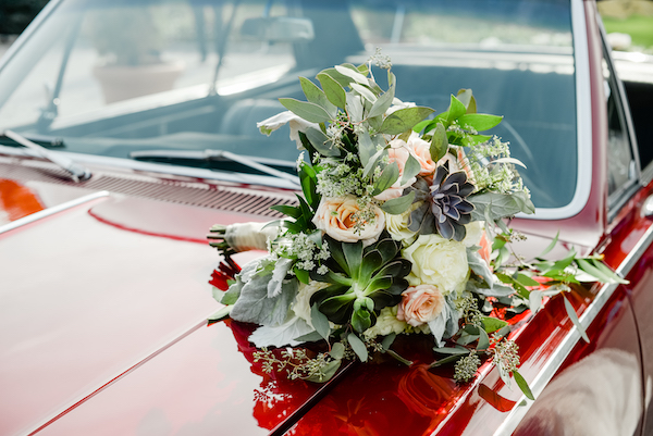 textured bridal bouquet with succulents and pink and white flowers sitting on a classic red Chevelle