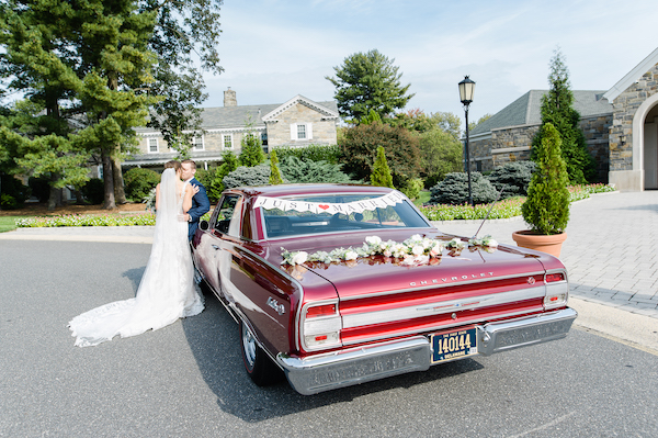 couple posing for photos in front of their classic red Chevelle with floral garland and Just Married sign