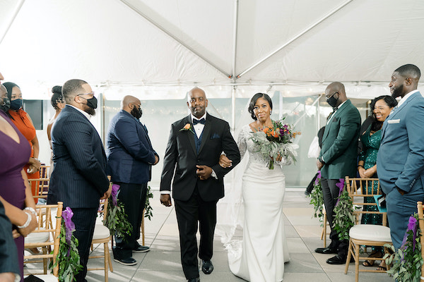 bride carrying a purple and orange bridal bouquet walking down the aisle at the Liberty View Ballroom