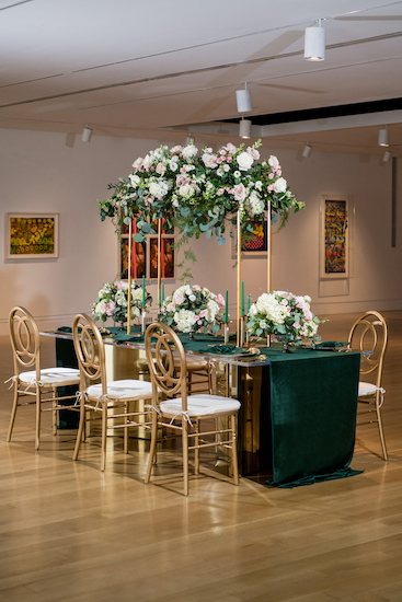modern gold and glass reception table draped in hunter green fabric with an overheard centerpiece on a gold riser