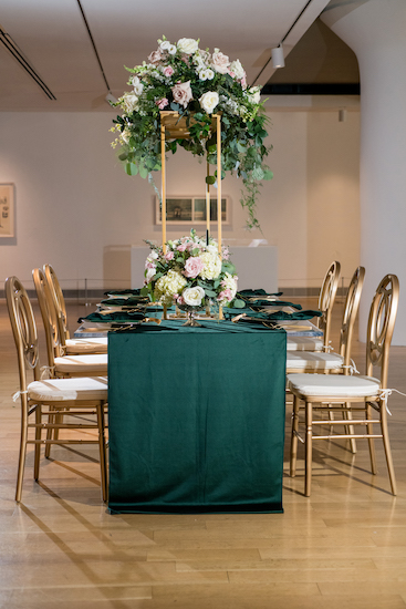 a long modern banquet table draped in hunter green with gold accents