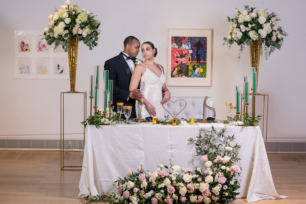 bride and groom standing in front of their hunter green and gold sweetheart table