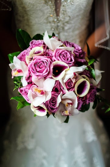 a brightly colored purple and white bridal bouquet with roses, orchids and calla lilies